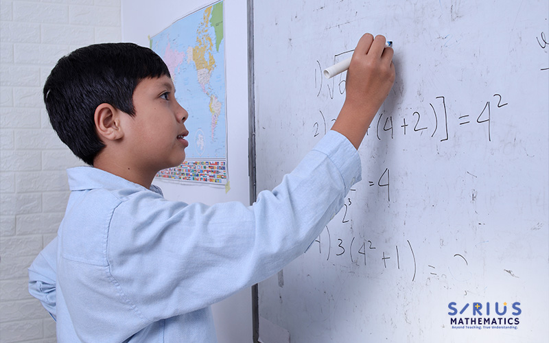 Boy writing math equations on a whiteboard.