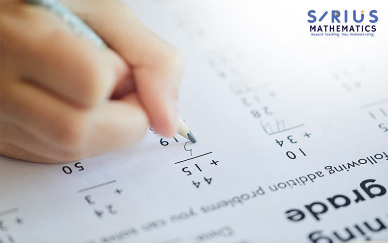 A student's hand solving a math problem on a test.